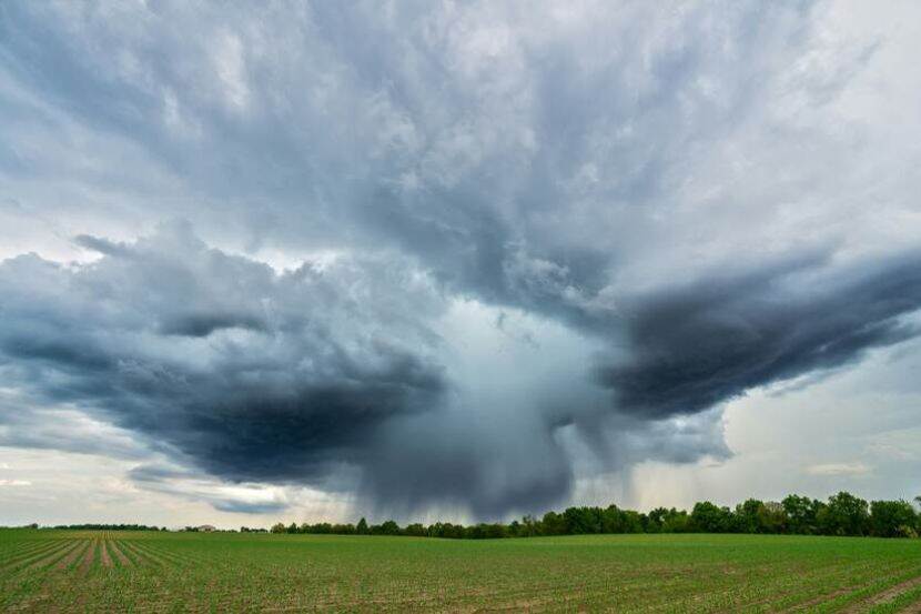 A flat green field with the horizon in the distance. Heavy cloud cover converges at a point on the horizon.