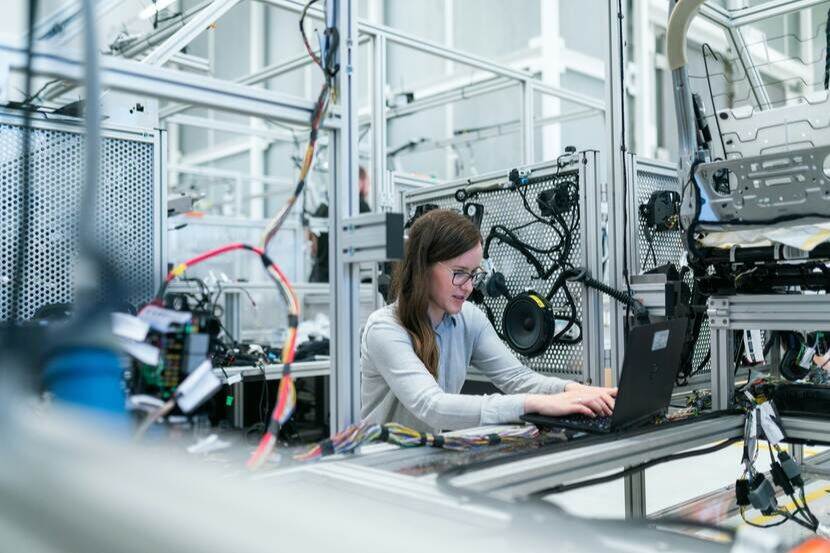 An engineer sits at a laptop in a lab surrounded by cables and ICT machinery and technology