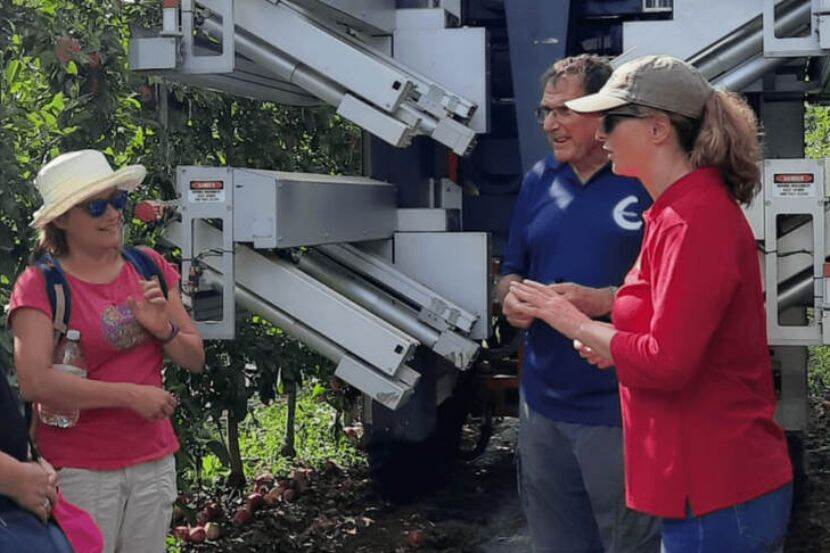 Three growers having a discussion and smiling near farming equipment. It is sunny and two growers are wearing sunglasses and hats.