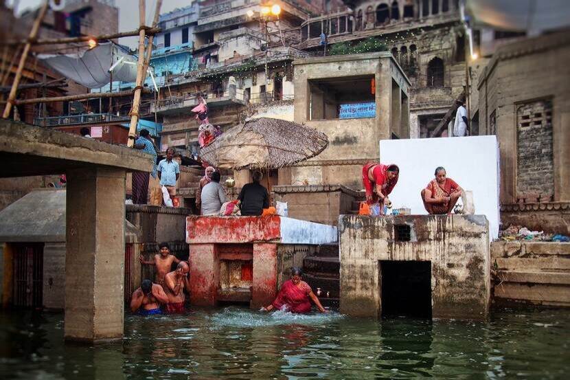 People bathe in a river in India. Steps and shanty houses surround the banks of the river.